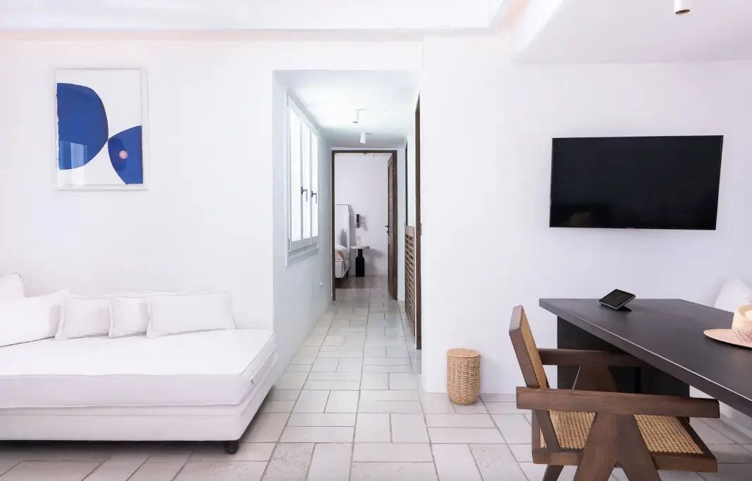 Heller Wohnbereich einer Suite mit Schreibtisch, Holzstuhl, weißem Liegesofa und Fliesenboden.