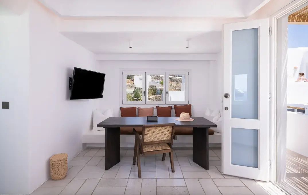 Essbereich mit dunklem Holztisch, Stuhl, Bank mit Kissen und Fernseher an der weißen Wand.
