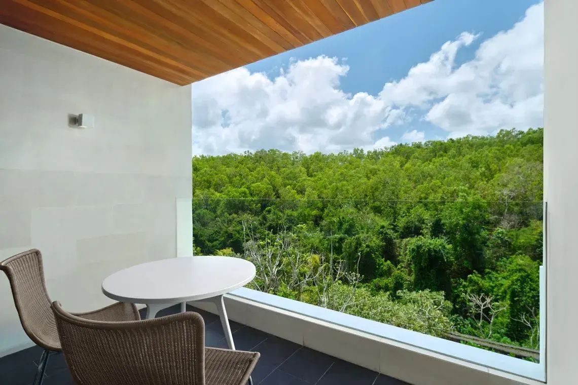 Balkon mit weißem Tisch und Stühlen sowie Blick auf einen dichten grünen Wald.