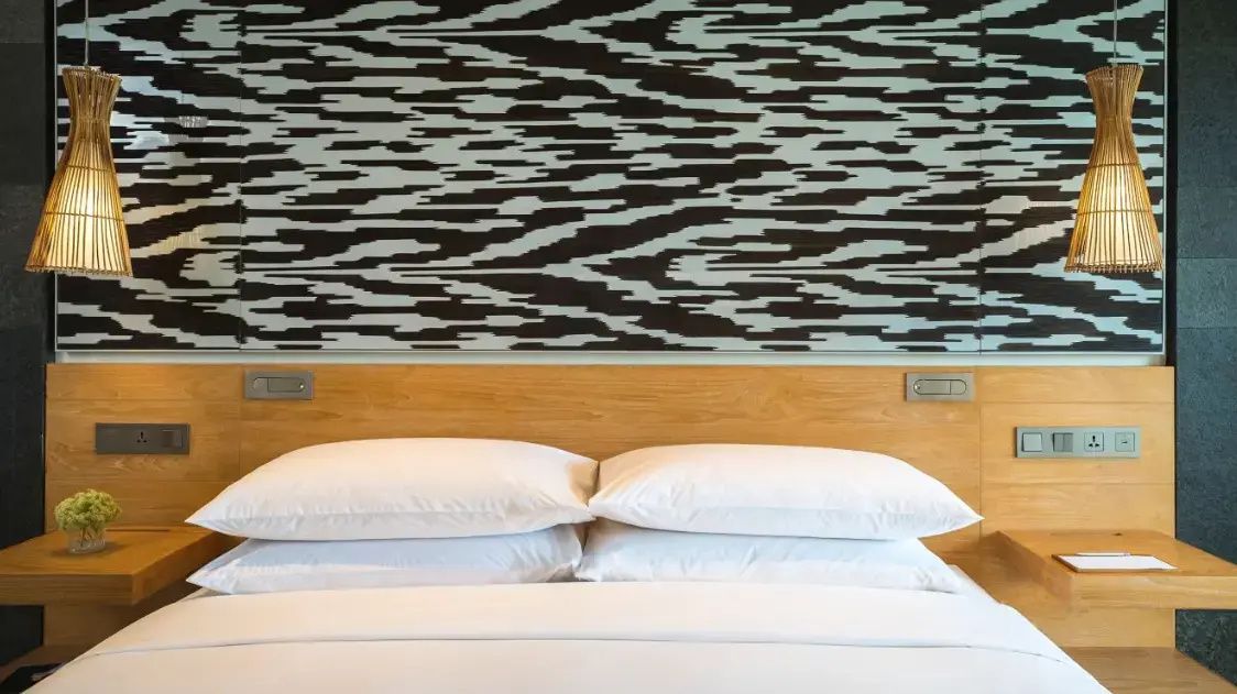 Weiß gekleidetes Bett mit zwei Kissen und gemusterter Wandgestaltung im Zimmer.