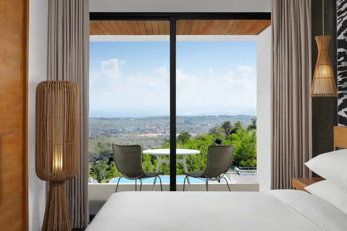 Blick durch eine große Glas Schiebetür auf einen Balkon mit zwei Stühlen und Aussicht auf die Landschaft.