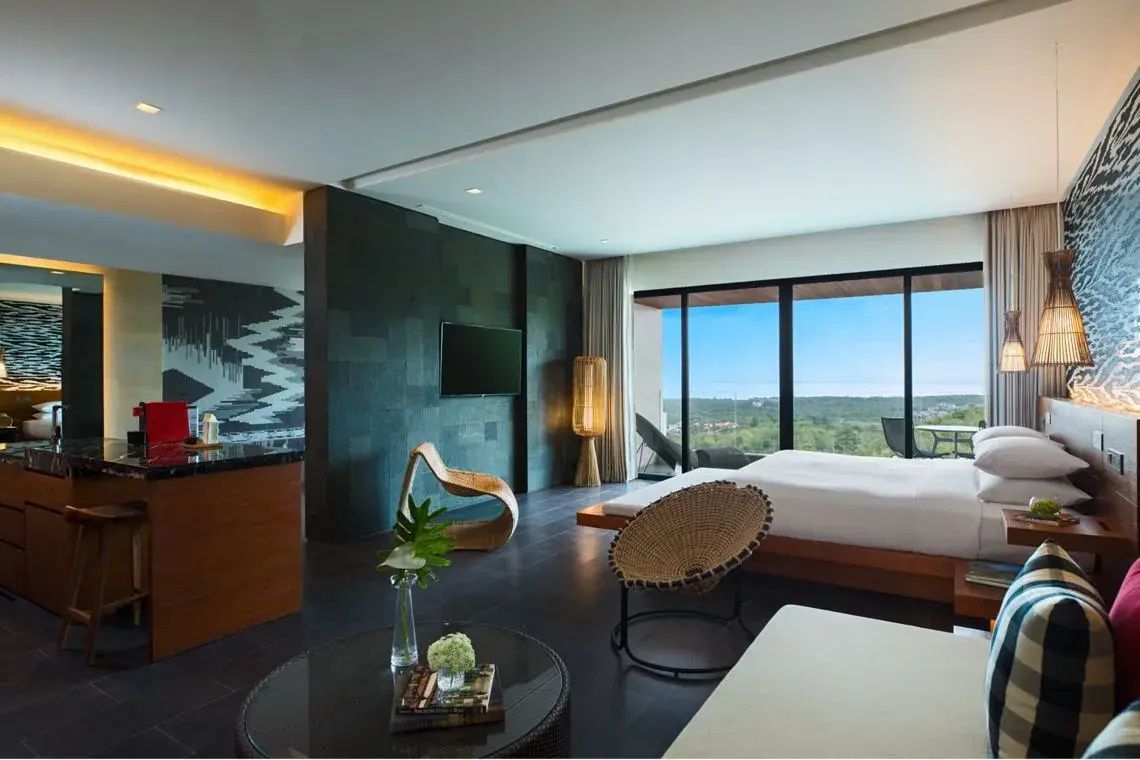 Hotelzimmer mit Doppelbett, Holzmöbeln, Fernseher und Fensterfront mit Blick auf die Natur.