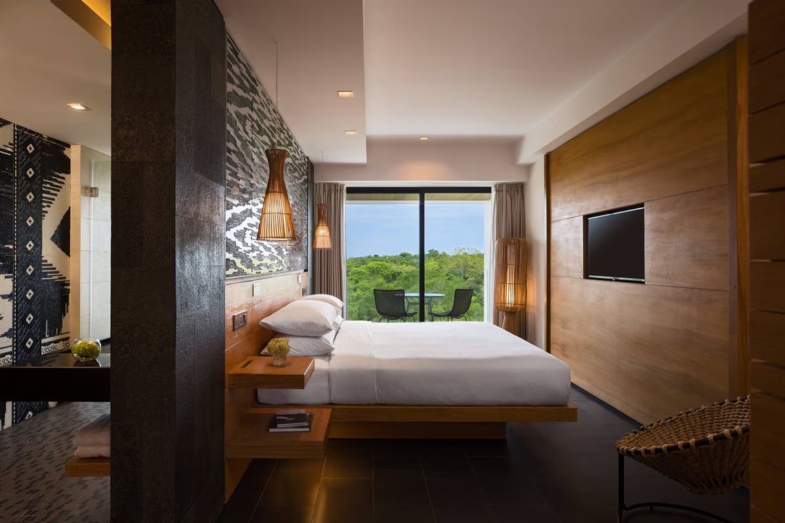 Modernes Hotelzimmer mit Doppelbett, Wand-TV und Blick auf grüne Natur.