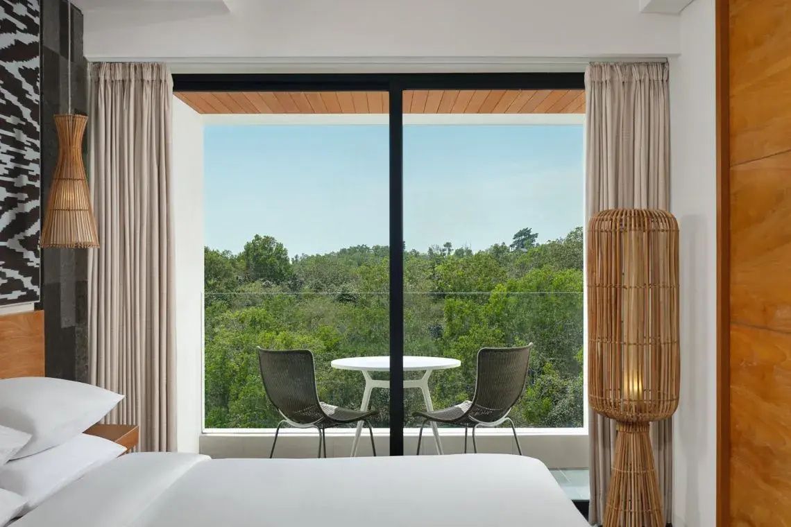 Blick vom Zimmer durch die Glasfront auf den Balkon und die umliegende Baumlandschaft.