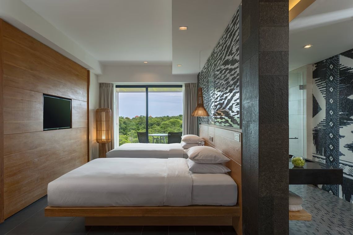 Hotelzimmer mit zwei Doppelbetten, Holzverkleidung und Blick ins Grüne durch eine Glasfront.