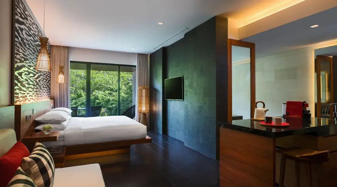Hotelzimmer mit großem Doppelbett, Fernseher an dunkelgrauer Wand und Blick ins Grüne.