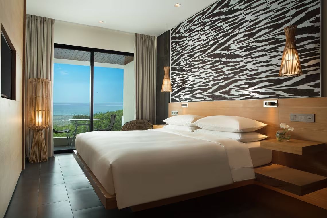 Hotelzimmer mit großem Doppelbett, gemusterter Wandgestaltung und Balkon mit Blick auf das Meer.