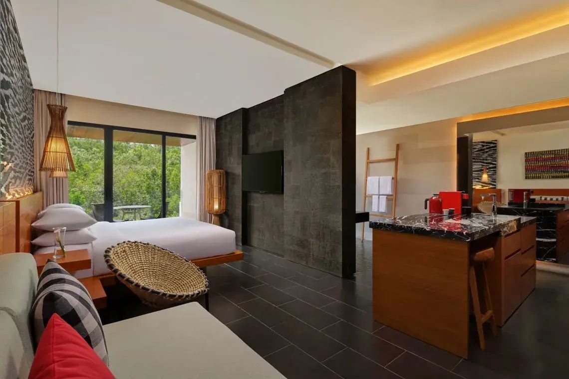 Modernes Hotelzimmer mit Doppelbett, dunklem Fliesenboden und Raumteiler mit TV.