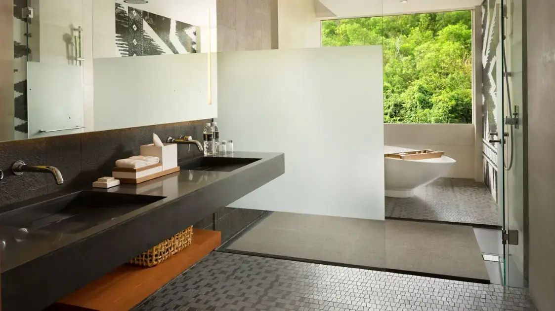 Badezimmer mit dunklem Waschtisch, Spiegel und freistehender Badewanne am Fenster.