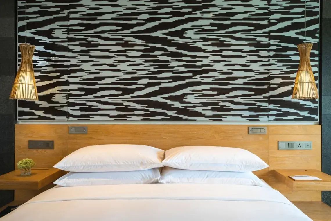 Weiches Bett mit weißen Kissen vor einer auffällig gemusterten Wand.