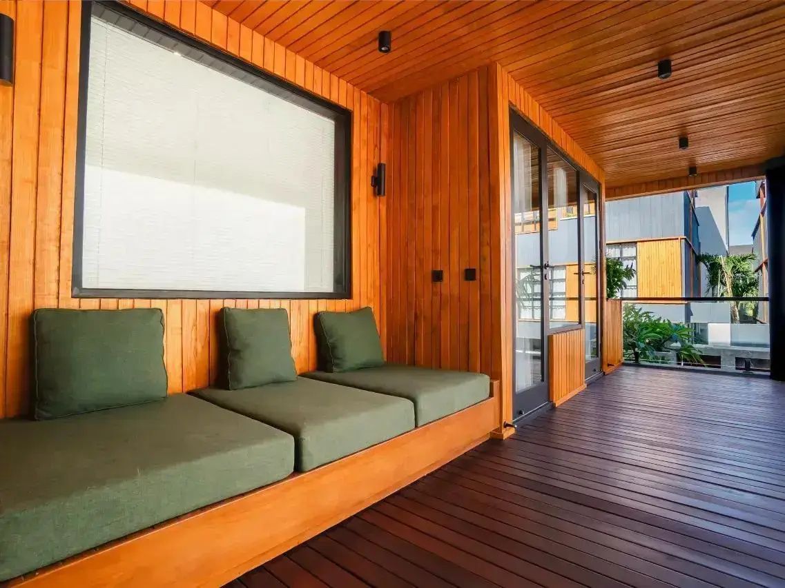 Überdachte Holzterrasse mit grünen Sitzpolstern und dunklem Dielenboden.