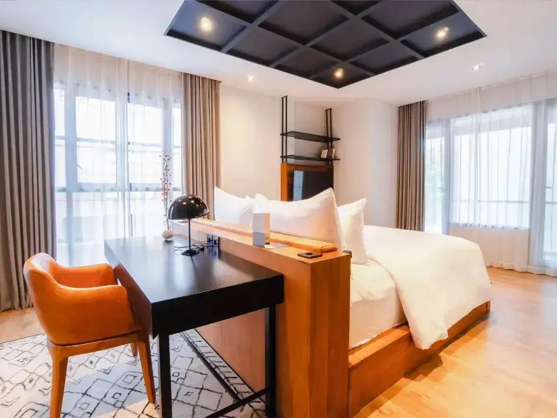 Schlafbereich mit Doppelbett, hölzerner Rückwand und Schreibtisch mit Stuhl.