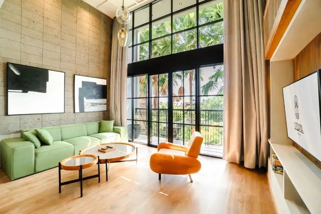 Wohnbereich mit grünem Sofa, orangem Sessel und hohen Fenstern zum Garten.