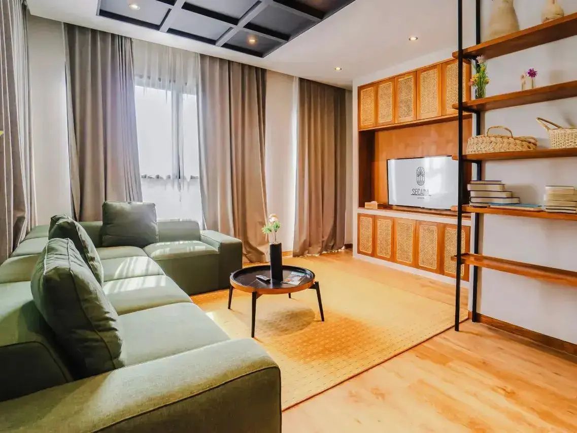 Wohnbereich mit grünem Ecksofa, rundem Couchtisch, Teppich und Fernsehwand.