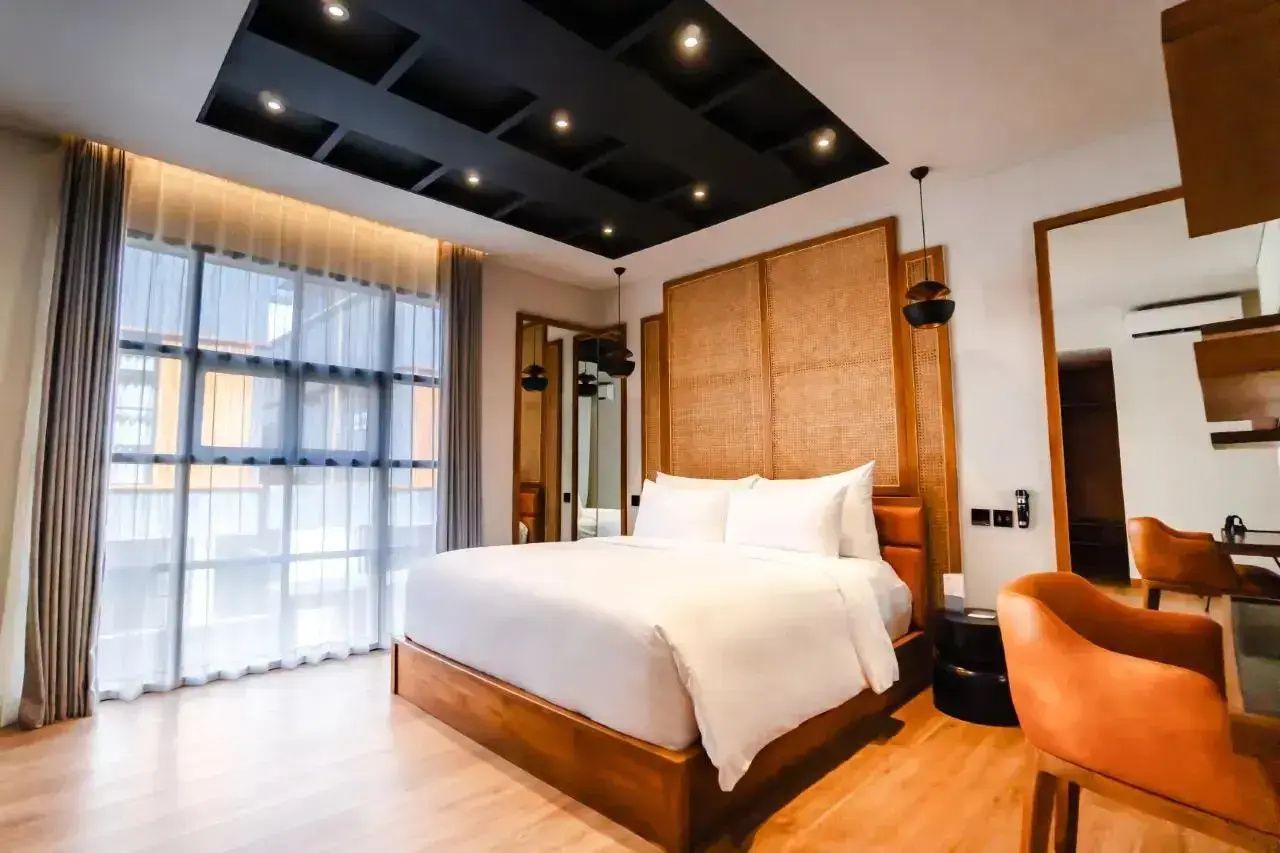 Helles Hotelzimmer mit großem Doppelbett, Holzkopfteil und dunkler Deckengestaltung.
