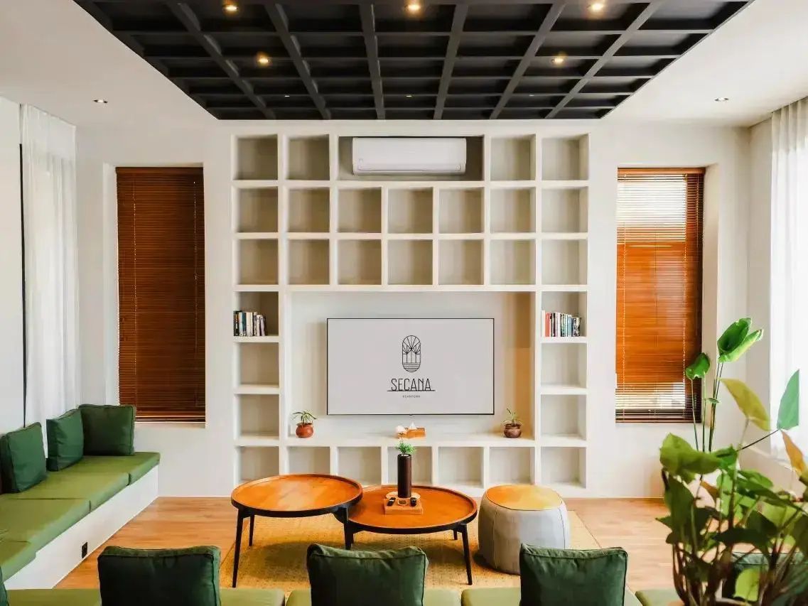 Wohnzimmer mit grünem Sofa, zwei runden Holztischen und weißer Regalwand.