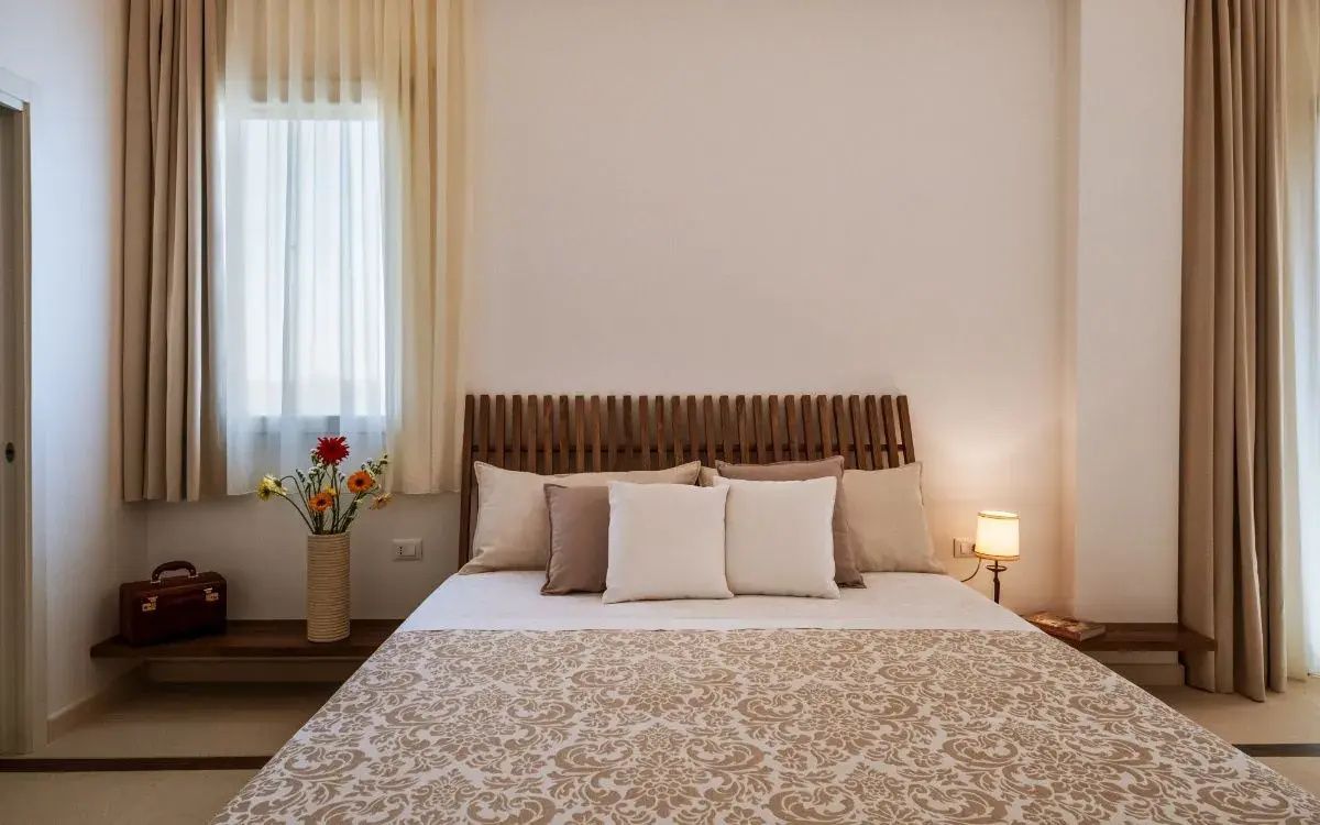 Doppelbett mit hölzernem Kopfteil, gemusterter Tagesdecke und bunten Blumen neben dem Nachttisch.