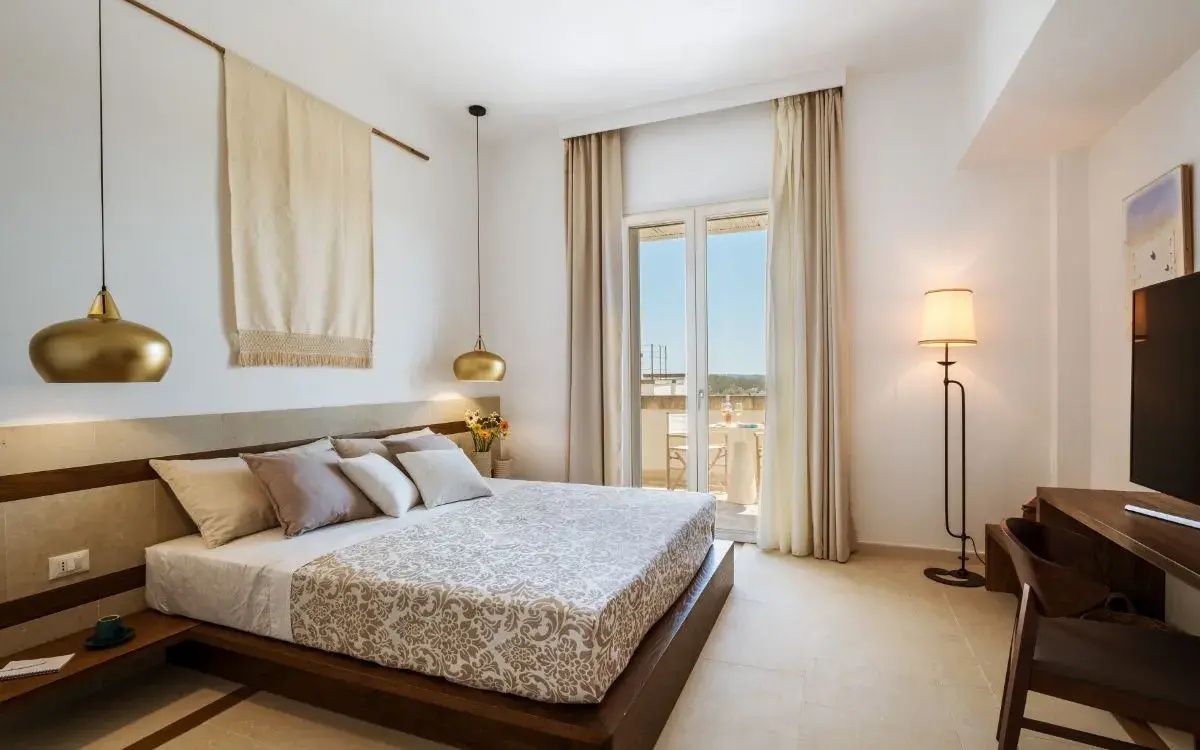 Helles Schlafzimmer mit Doppelbett, Vorhängen und Zugang zu einer Sonnenterrasse.