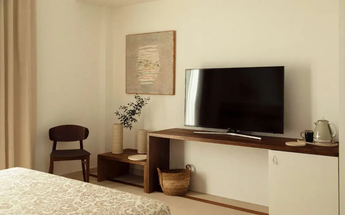 Holztisch mit Flachbildfernseher, Holzstuhl und Wandbild in einem hell eingerichteten Zimmer.