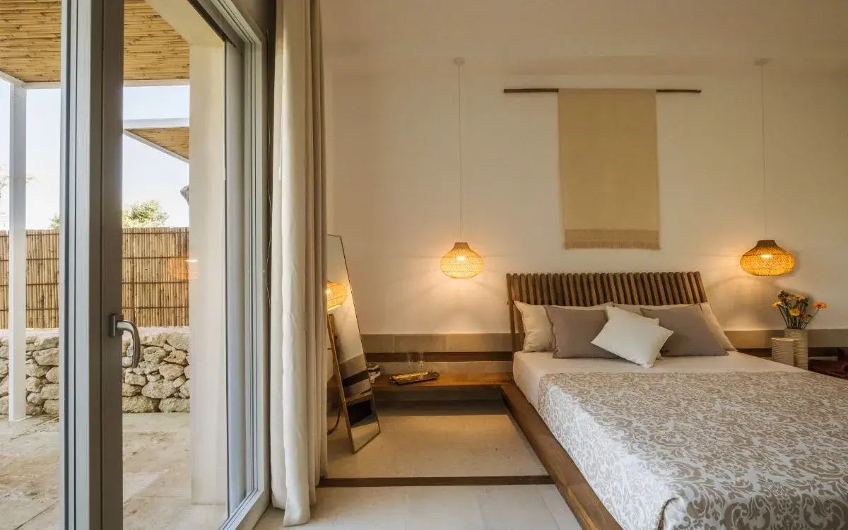 Helles Hotelzimmer mit Doppelbett, großem Spiegel und einer Balkontür mit Vorhang.