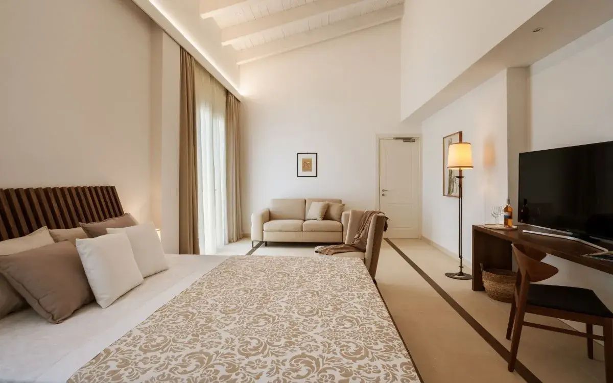 Hell gestalteter Wohnbereich und Schlafbereich mit hoher Decke sowie beigefarbenem Sofa und Sessel.