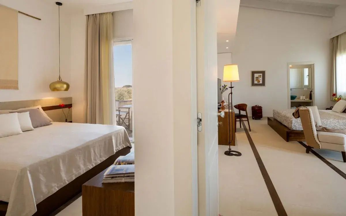 Blick durch die Suite auf ein Doppelbett, eine Stehlampe und eine Balkontür ins Freie.