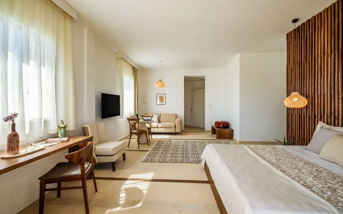 Geräumiges Zimmer mit Bett, Fernseher an der Wand, Sofa und Teppich auf hellem Fliesenboden.