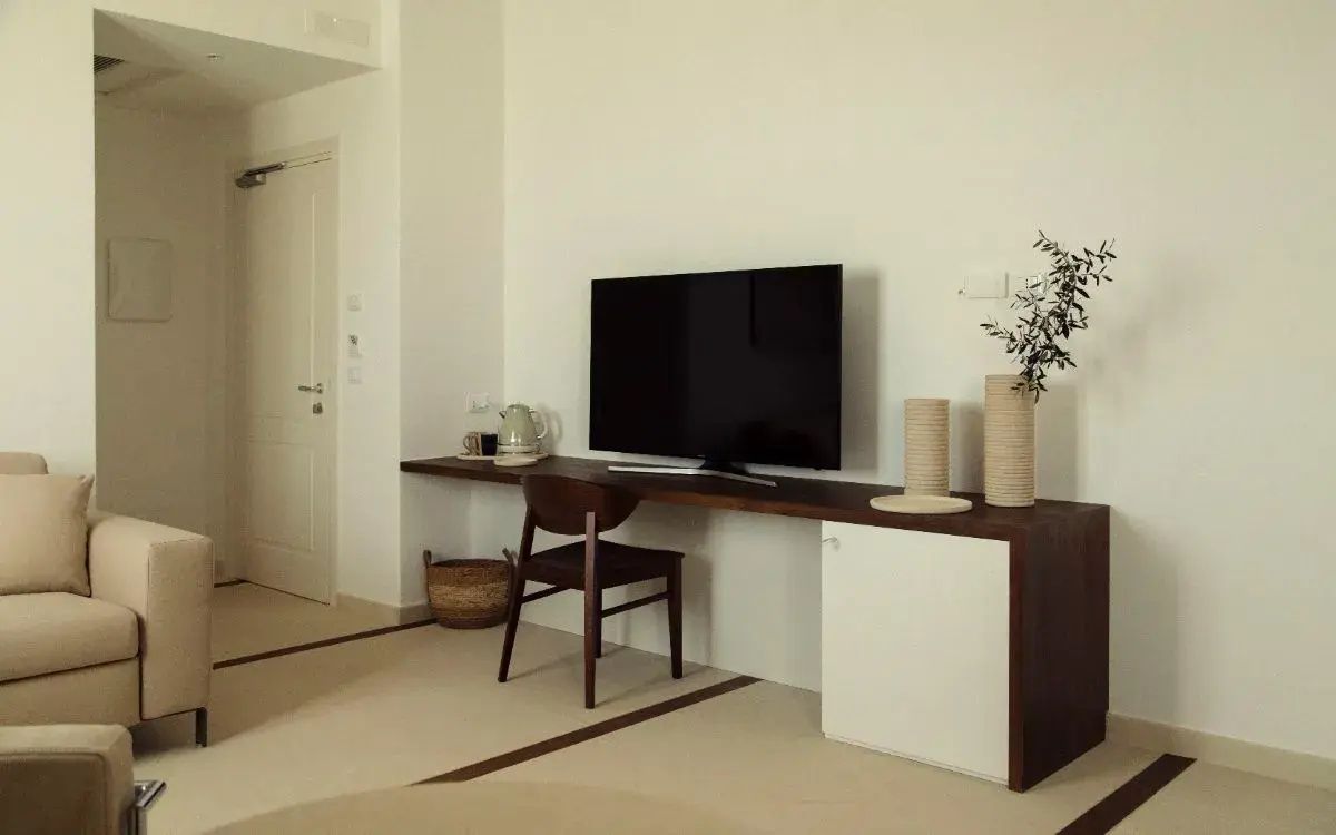 Langer Holzschreibtisch mit Fernseher, Stuhl und Wasserkocher in einem hellen Zimmer.