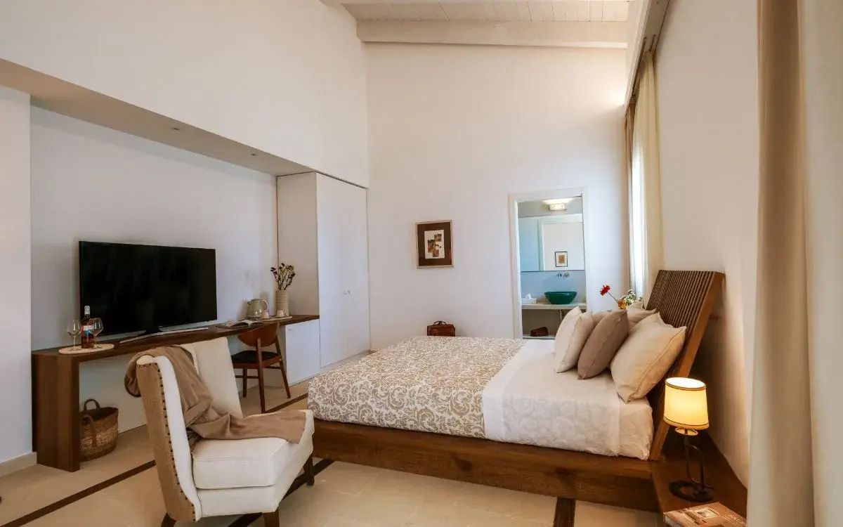 Hell eingerichtetes Hotelzimmer mit Doppelbett, Fernseher auf dem Tisch und Blick ins Badezimmer.