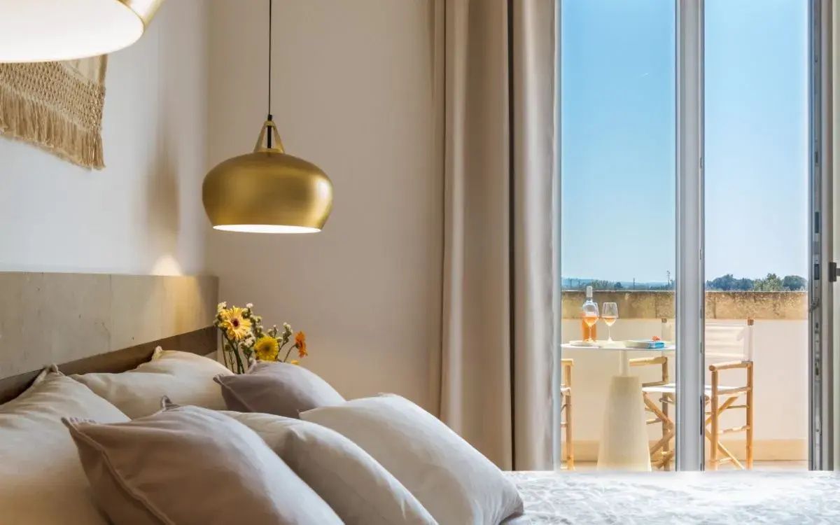 Blick über das Bett mit goldener Lampe durch die Balkontür auf den Außenbereich.