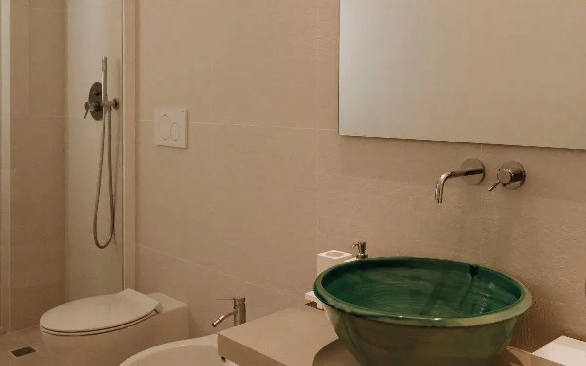 Modernes Badezimmer mit grünem Aufsatzwaschbecken, Spiegel und Bidet in hellen Tönen.