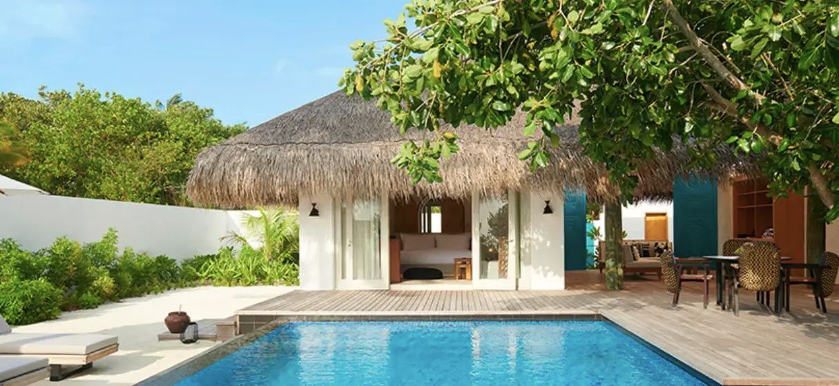Reetgedeckte Strandvilla mit privatem Pool auf der Holzterrasse und geöffneten Türen zum Schlafbereich.