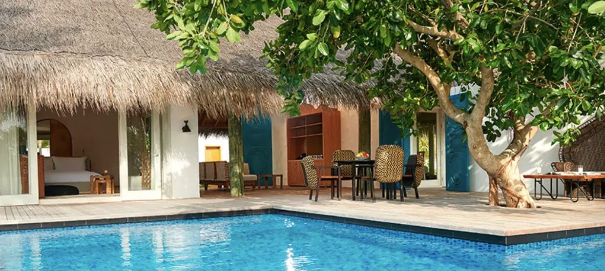 Überdachte Terrasse einer Villa mit Esstisch, Sitzgelegenheiten und Swimmingpool im Vordergrund.