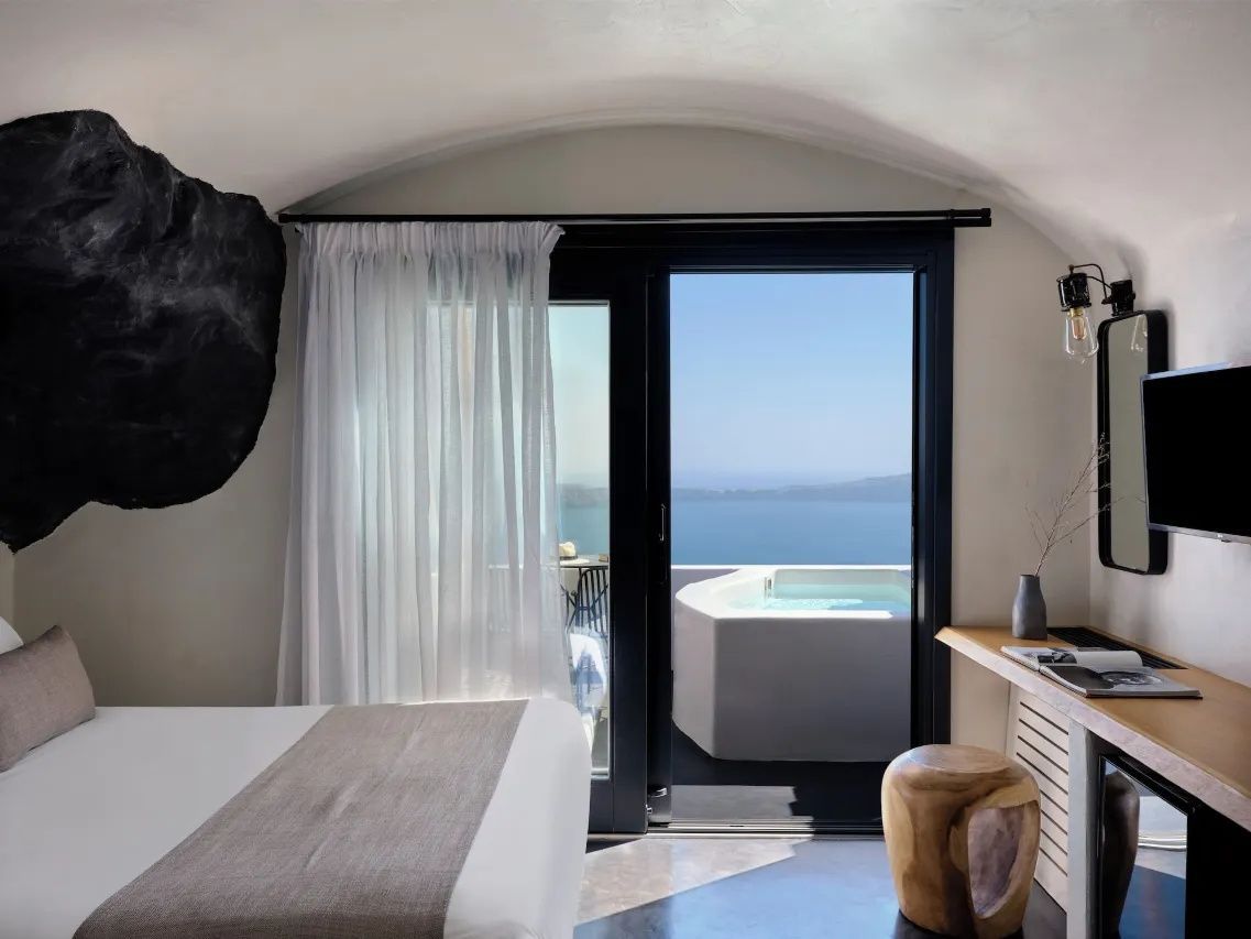 Blick aus dem Zimmer auf die Terrasse mit Jacuzzi und das Meer im Hintergrund.
