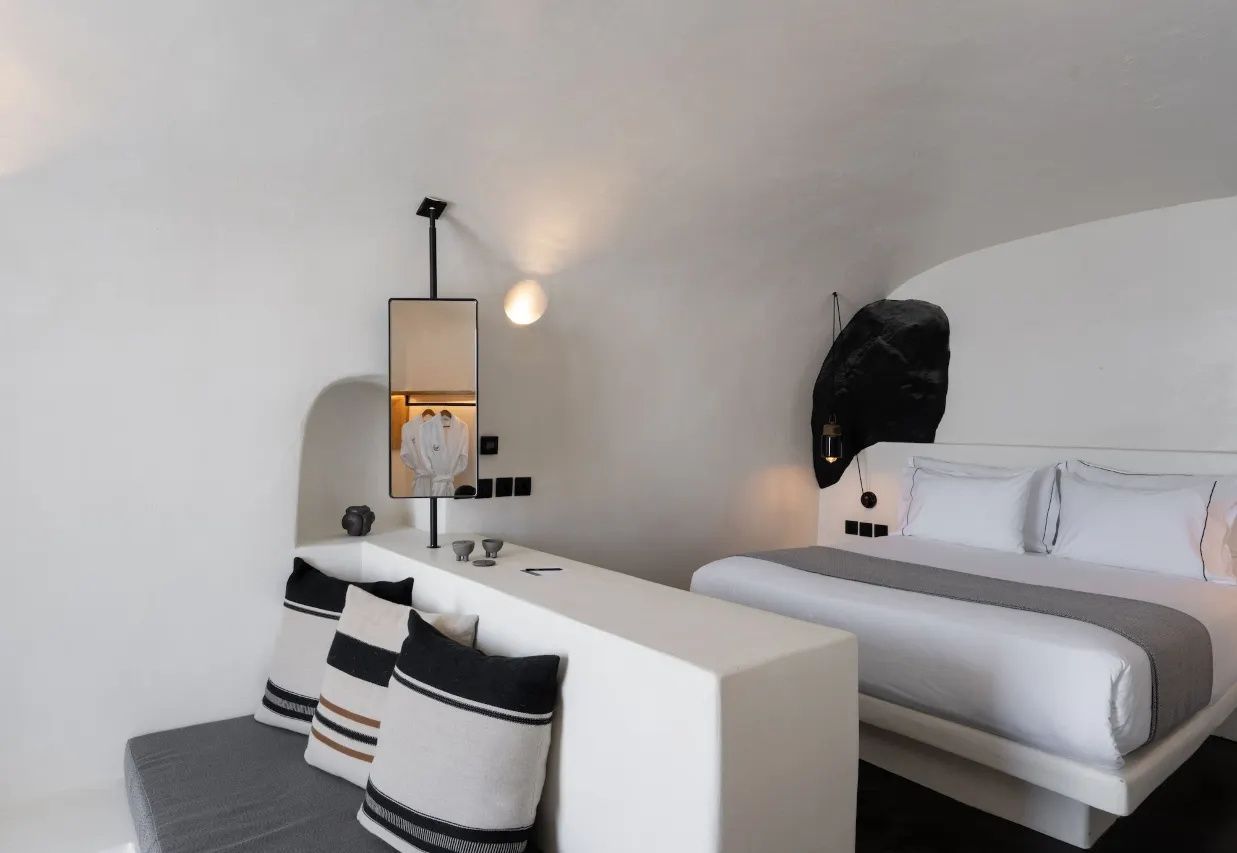 Schlafbereich mit weißem Doppelbett, Sitzecke und Raumteiler in Höhlenoptik.
