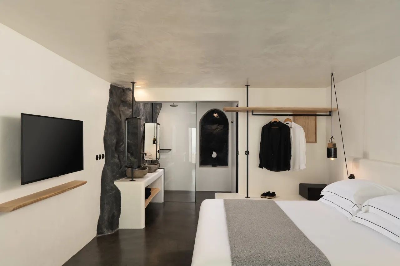 Hell gestaltetes Hotelzimmer mit Doppelbett, Kleiderstange und offenem Badezimmerbereich.