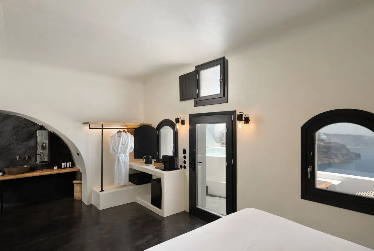 Weiß eingerichtetes Hotelzimmer mit offenem Kleiderständer, Bademantel und dunklem Boden.