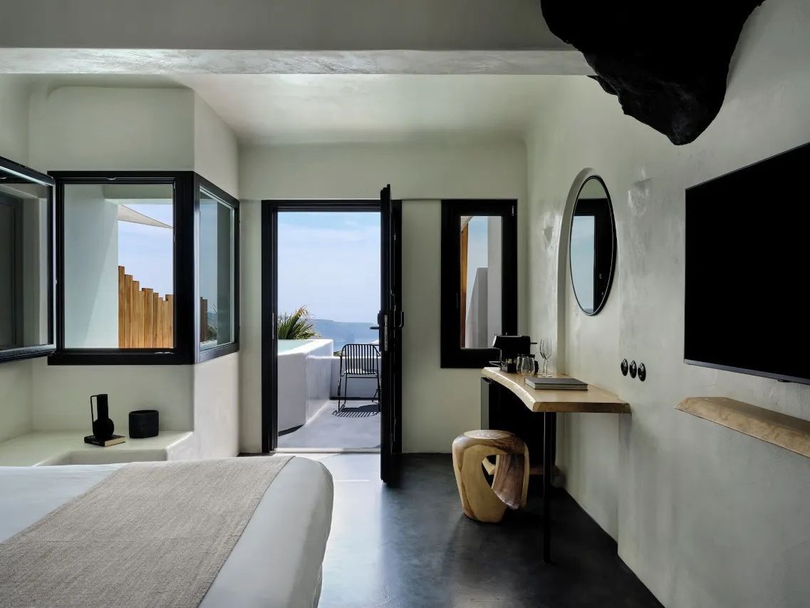 Hell gestaltetes Hotelzimmer mit Holztisch, Spiegel und Blick auf eine Terrasse mit Whirlpool.