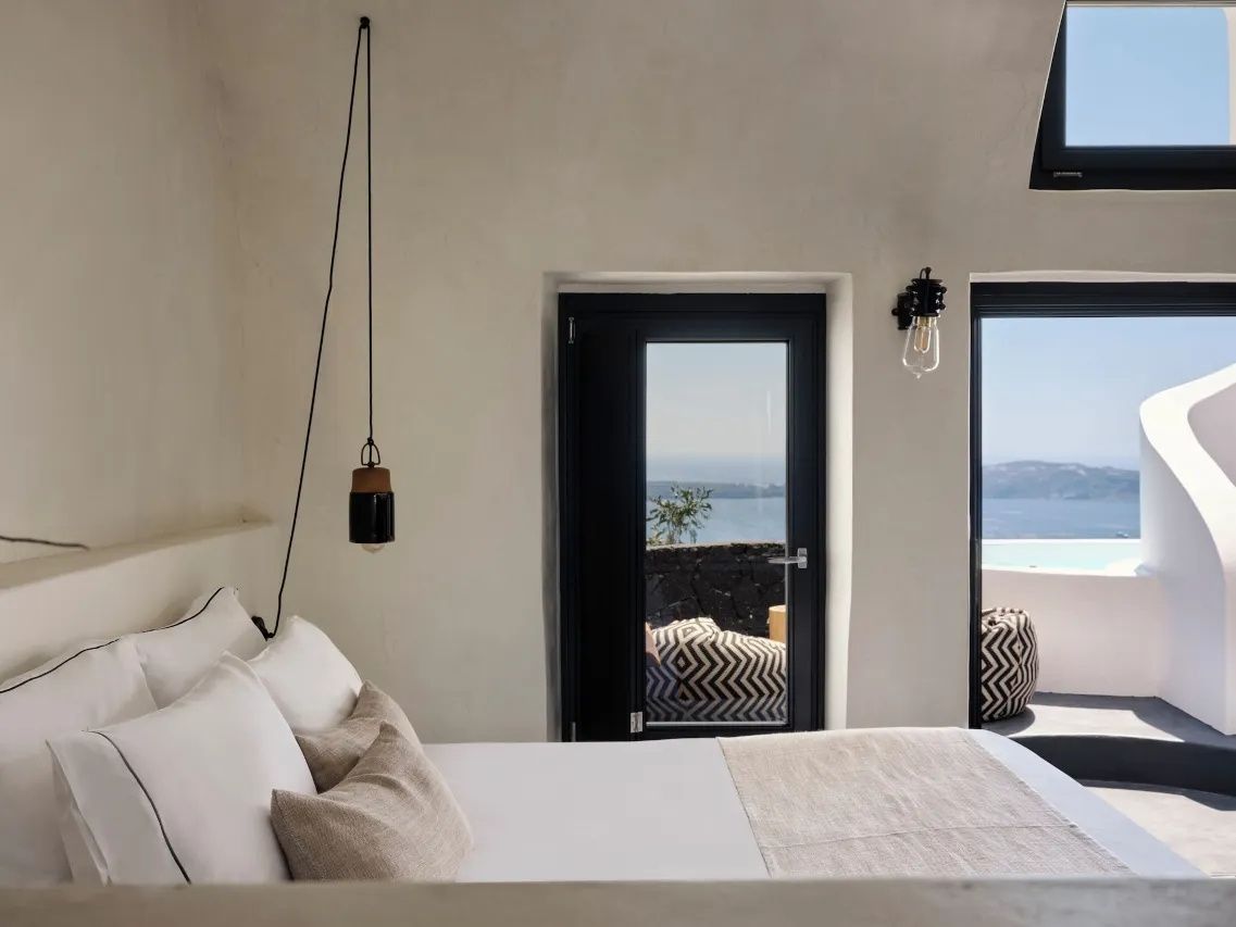 Weiss eingerichtetes Schlafzimmer mit Doppelbett und Blick durch die Balkontuer auf das Meer.