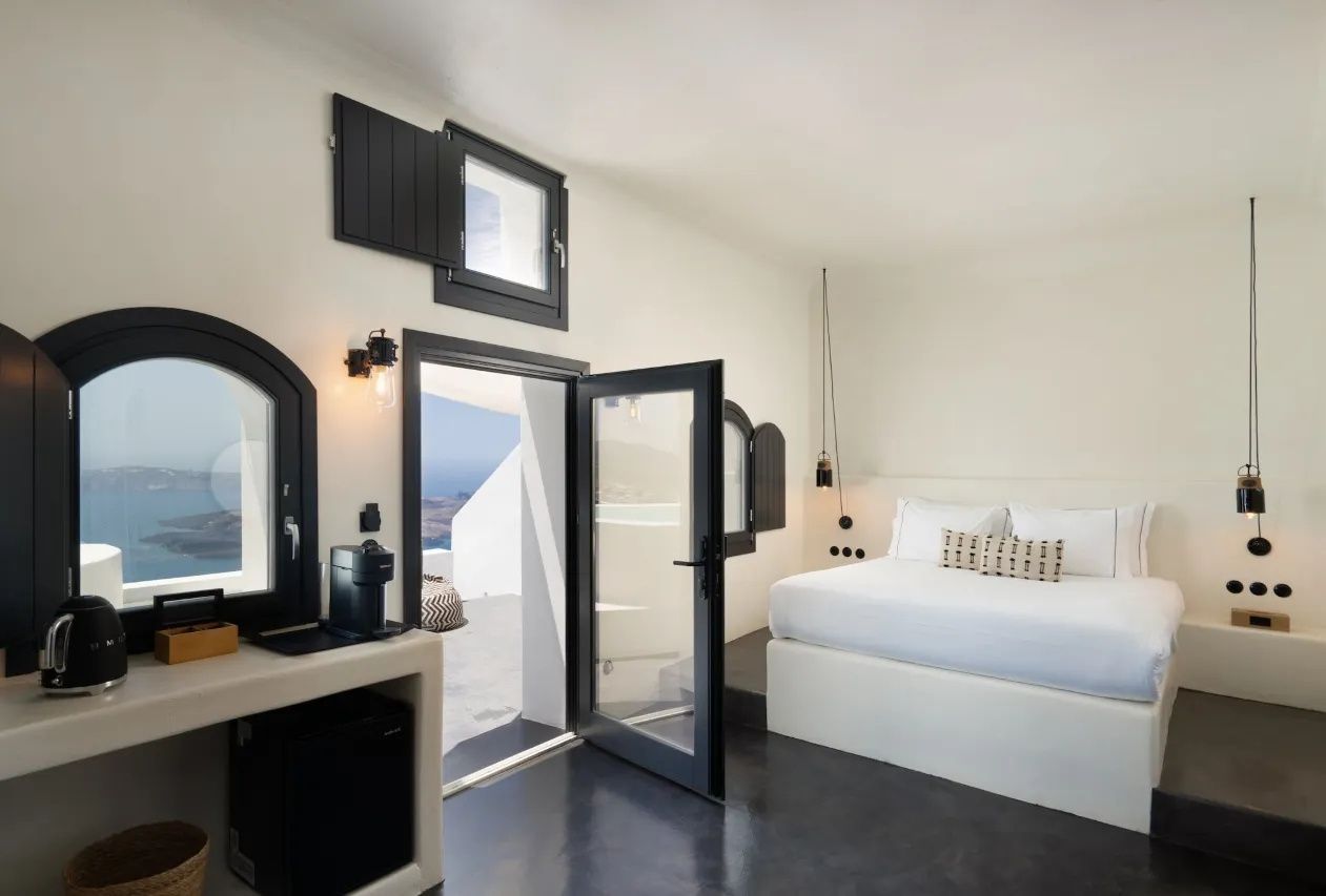 Hell gestaltetes Schlafzimmer mit weißem Doppelbett und geöffnete Tür zur Terrasse.