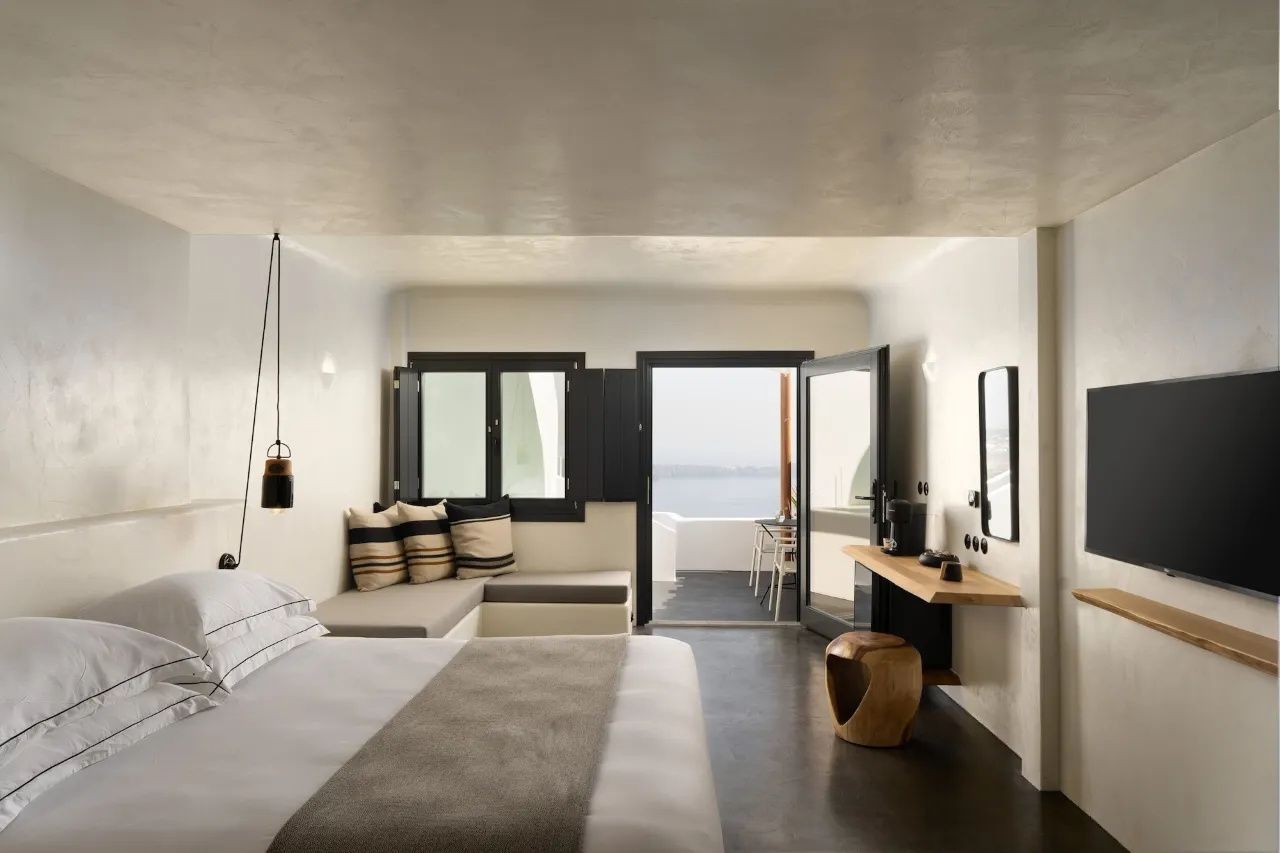 Hotelzimmer mit Doppelbett, Sitzbereich und geöffneter Tür zur Terrasse mit Meerblick.