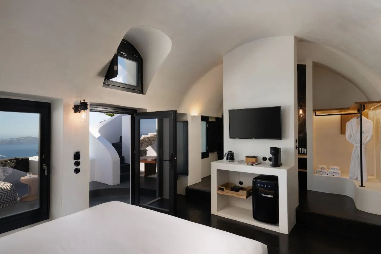 Hell gestaltetes Hotelzimmer mit Doppelbett, Fernseher und Zugang zur privaten Terrasse.