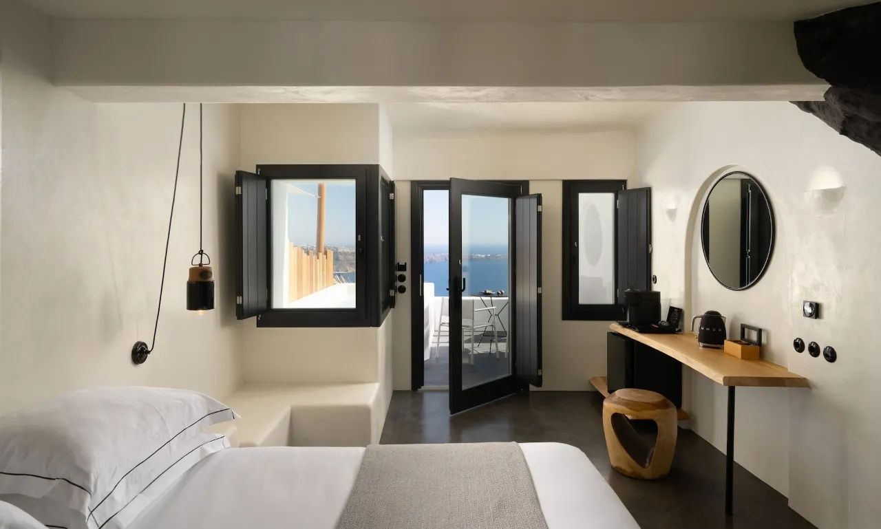 Helles Zimmer mit Doppelbett, dunklen Fenstern und Ausblick auf das Meer und die Terrasse.