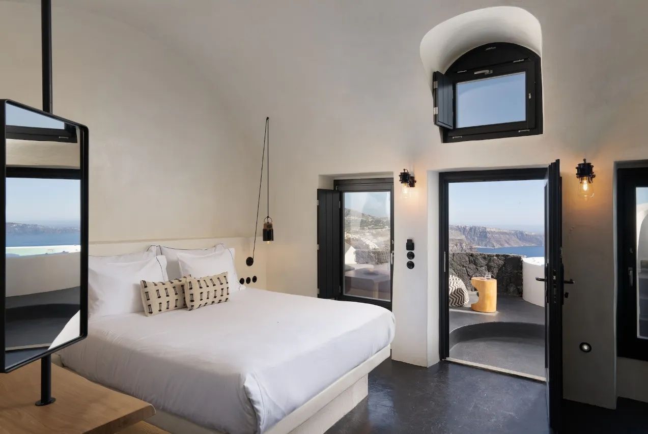 Schlafbereich mit weissem Bett, Gewoelbedecke und Blick auf die Terrasse und das Meer.