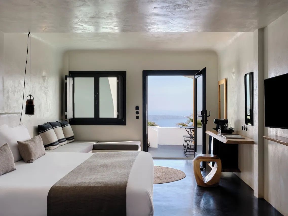Modernes Zimmer mit Doppelbett, Ecksitzbank und freiem Blick auf das Meer durch die Balkontür.