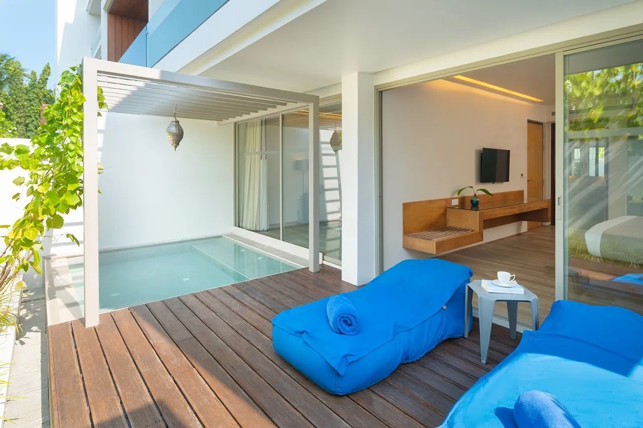 Holzterrasse einer Villa mit kleinem Pool, überdachtem Bereich und blauen Liegekissen.