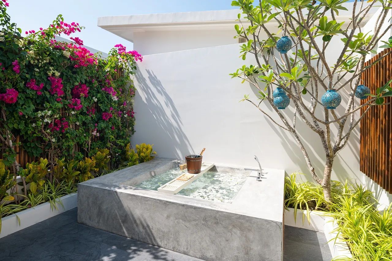 Eckiger Whirlpool aus Beton auf einer Terrasse mit tropischen Pflanzen und weiße Wand.