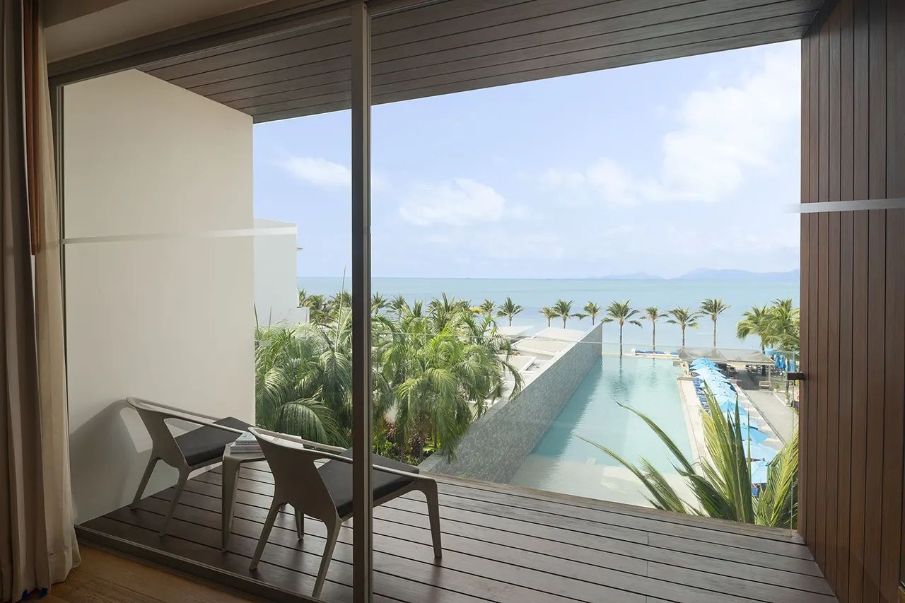 Balkon mit Holzfußboden und zwei Stühlen sowie Aussicht auf den Pool und das Meer.