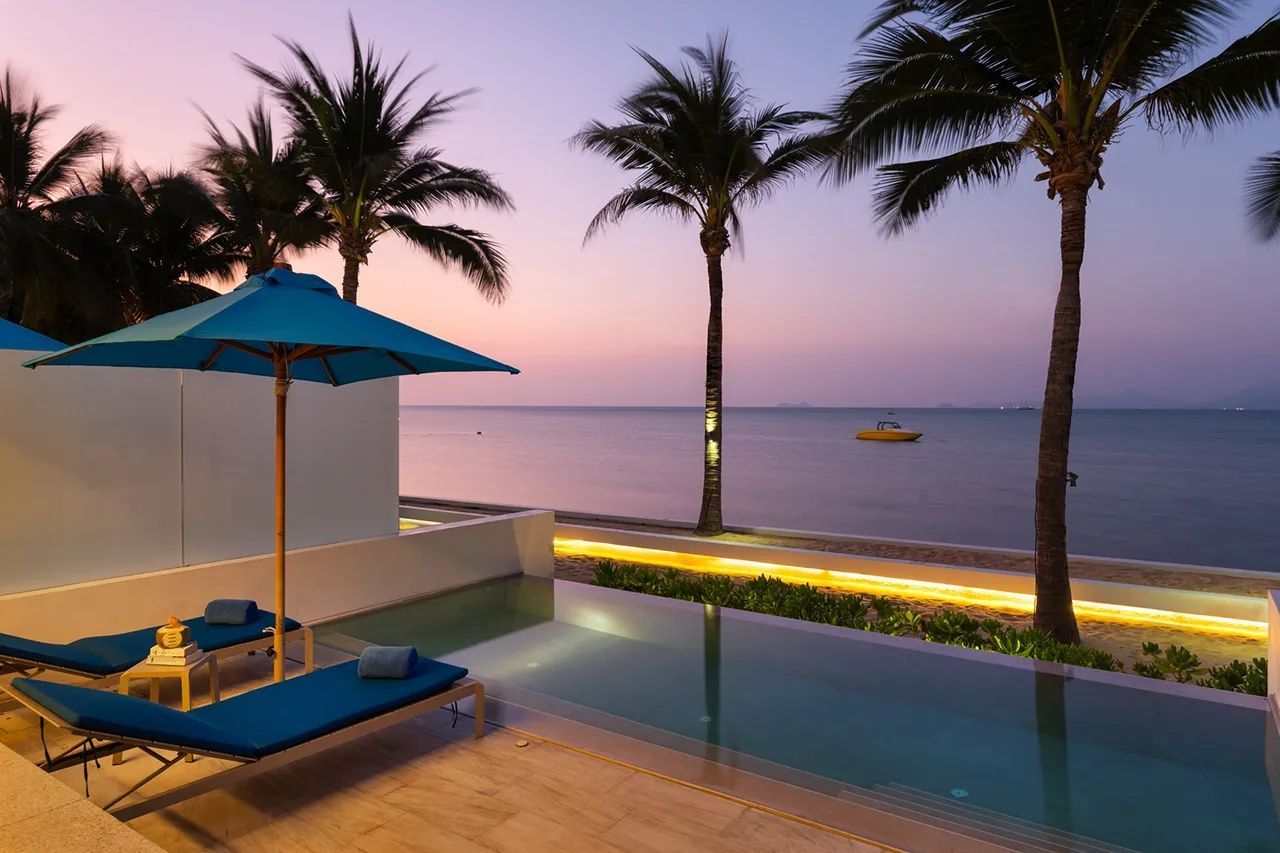 Terrasse mit eigenem Pool, Sonnenschirm und Liegestühlen am Meer bei Dämmerung.