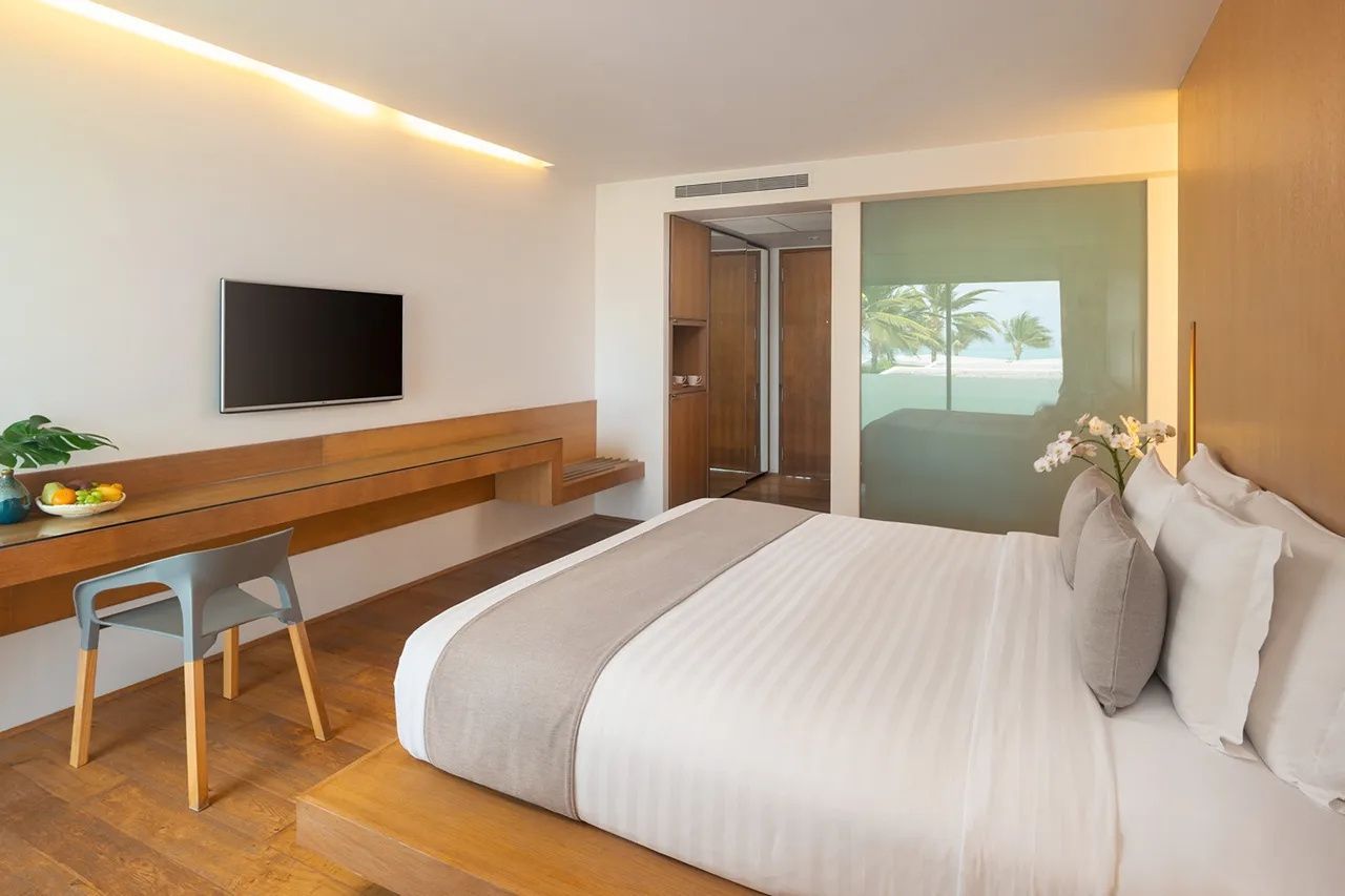 Modernes Hotelzimmer mit grossem Doppelbett, Fernseher an der Wand und Schreibtisch aus Holz.